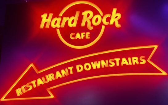 Illuminated writing in red saying Hard Rock Cafe Restaurant downstair with an arrow which is also illuminated in red. it is glowing