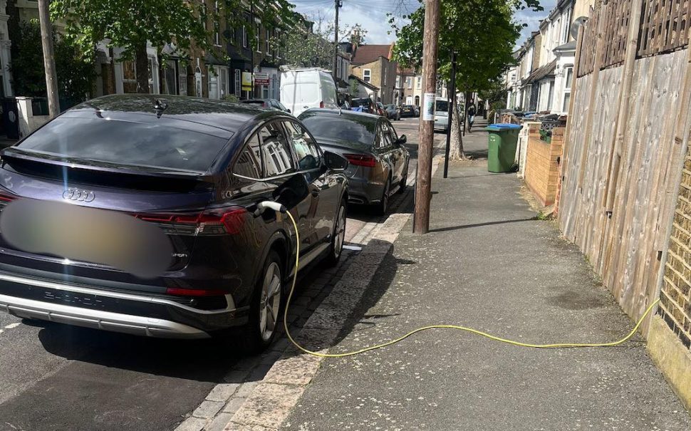 Yellow cable trailing across pavement plugged into black car