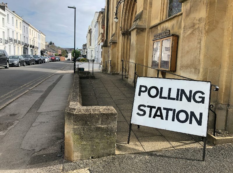 A sign reading "Polling Station" is set outside a ramped entrance to a building on a quiet street.