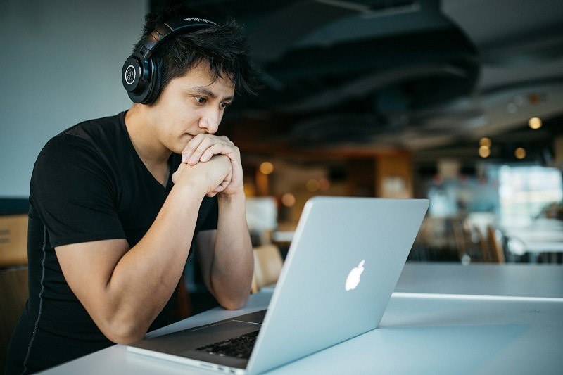 A young man looking at his laptop, wearing his headphones