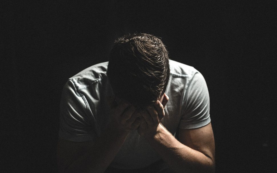 Man sat with his head in his hands, outlining effects of male domestic abuse