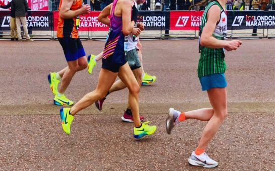 Runners in motion wearing multi-coloured gym clothes. The image cuts off their heads. In the background are barriers with TCS London Marathon text written across them.