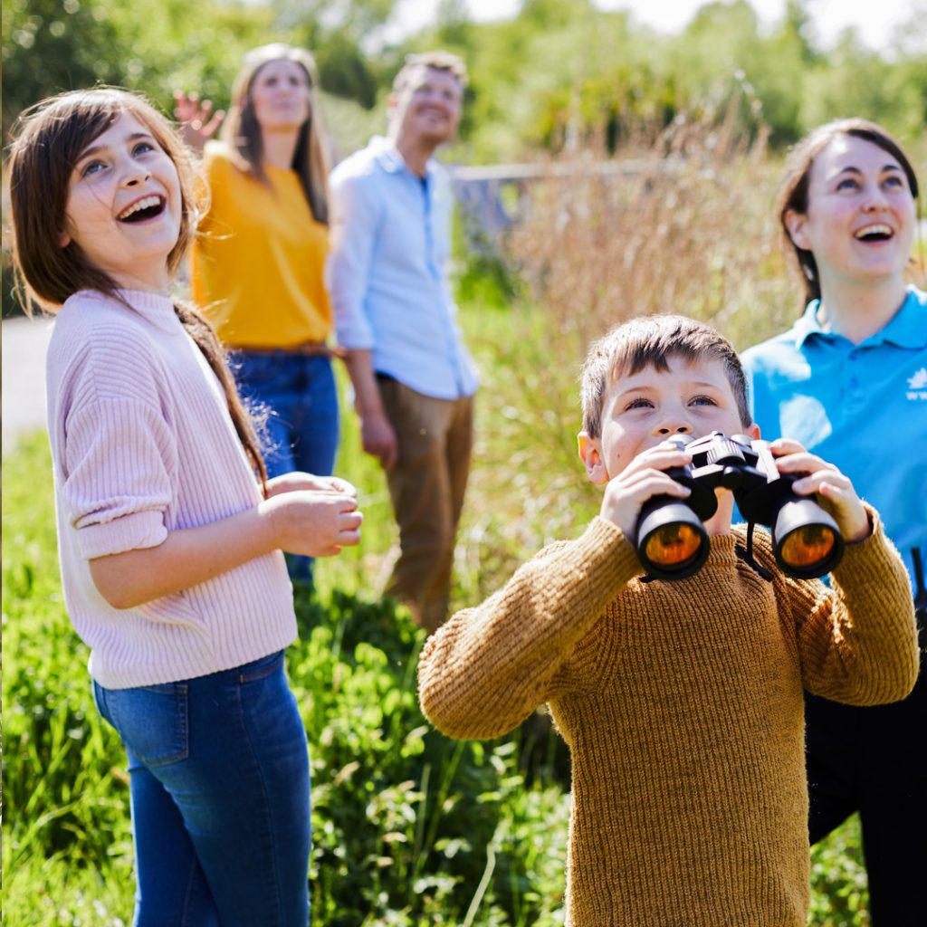 A family looking at something in the sky off camera, with one holding binoculars