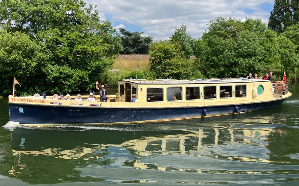 A yellow and blue boat on the river, with a man waving towards the camera