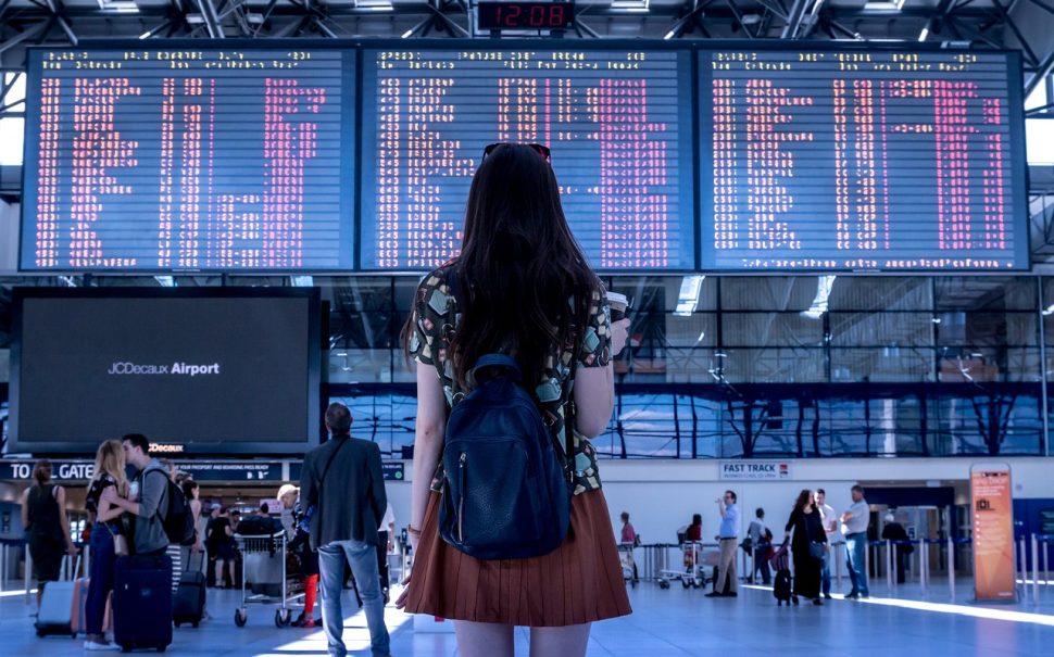 A woman stands in front of airport departure boards