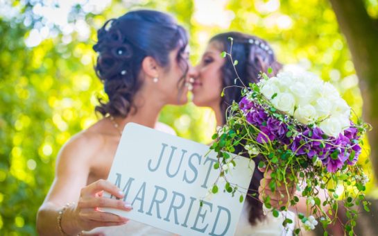 Brides kissing behind a 'just married' sign