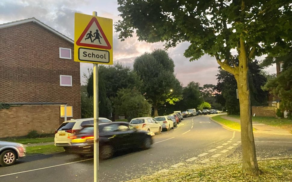 A car speeds past a school hazard sign on the side of a road in Ham