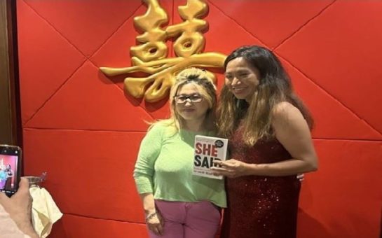 Rowena Chiu stood up smiling with another woman to her left, holding the book "She Said", in which her story is featured.