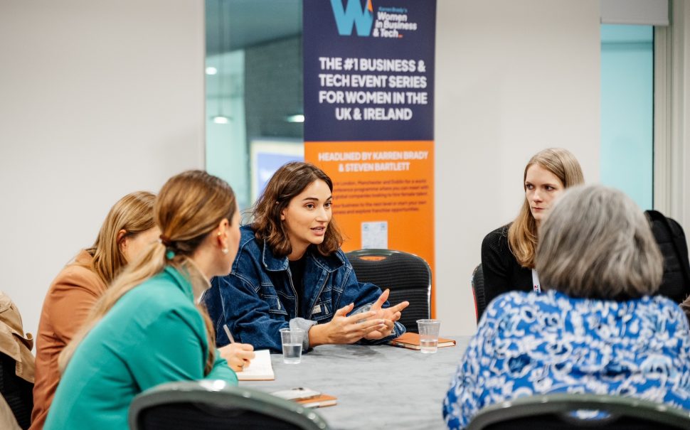 A panel of women sit around a table discussing business at the Women in Business & Tech event.