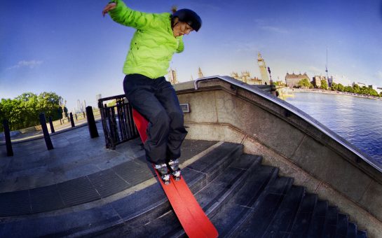 A freeride skier riding down a set of stairs on red skis next to the Thames