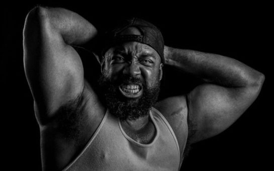 Man holding large muscular arms behind his head and bearing his teeth.