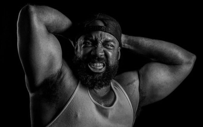 Man holding large muscular arms behind his head and bearing his teeth.