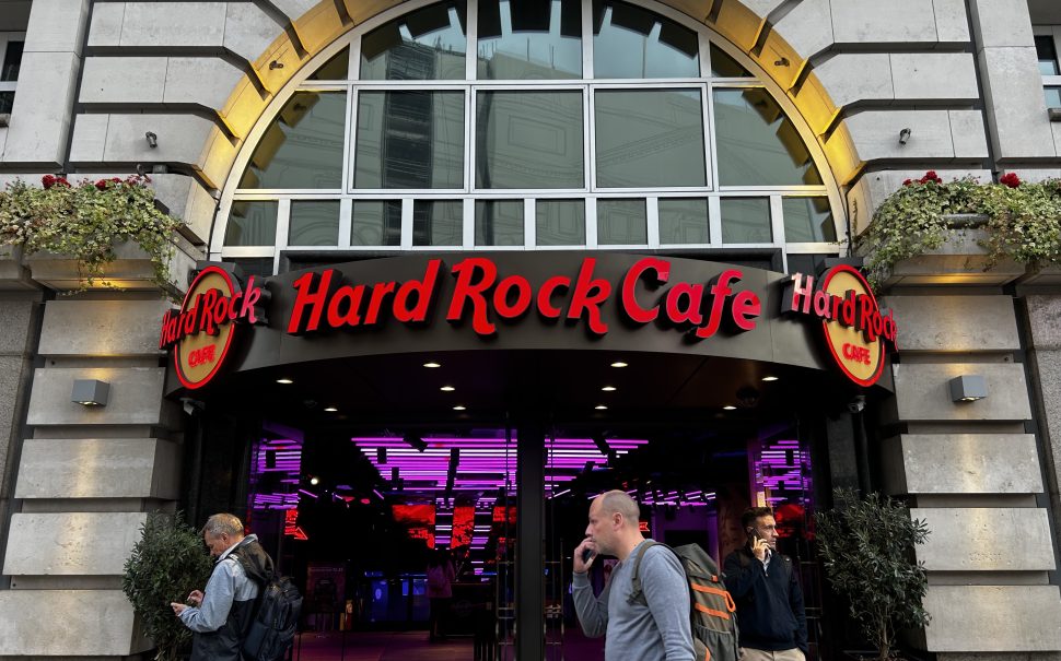 Hard Rock Cafe Piccadilly store front, red illuminated text saying Hard Rock Cafe there is people walking infant of the front.