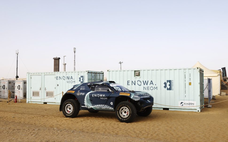 An Extreme E SUV next to two shipping containers all decorated with ENOWA branding, a partnership recognised by the sustainability nomination