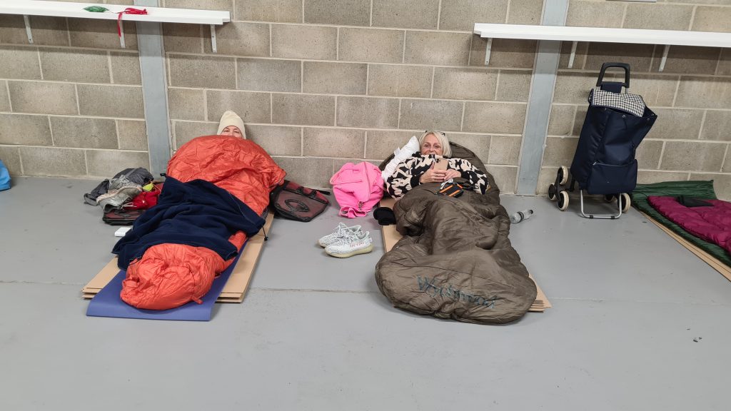 Two sponsored participants lay on cardboard, wrapped in sleeping bags for the night