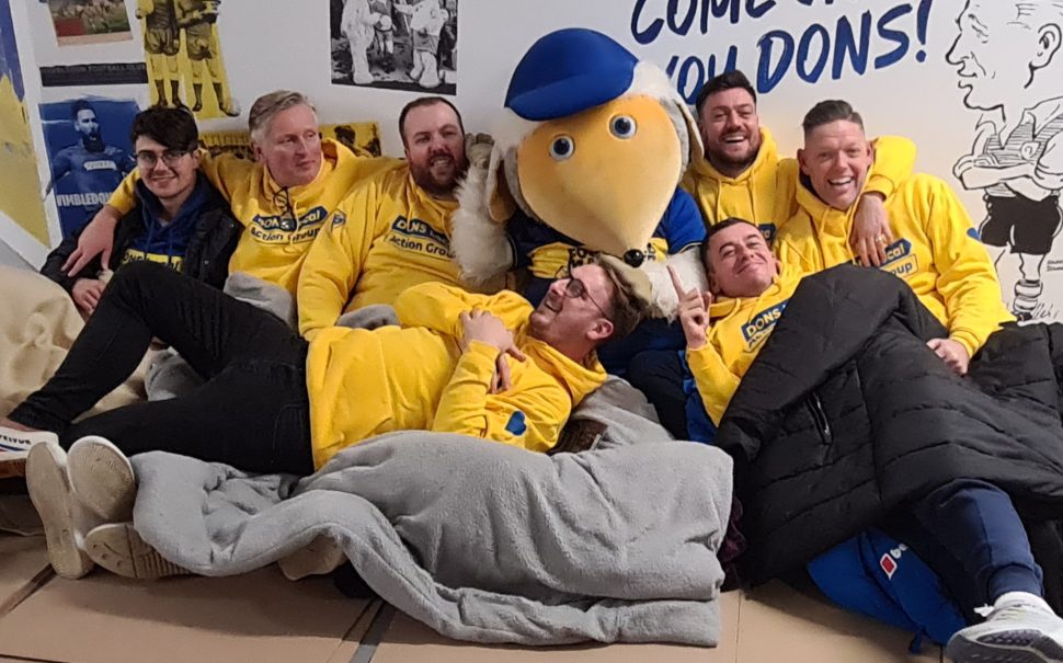 Sponsored participants cuddle up with AFC Wimbledon’s mascot on the stadium floor.