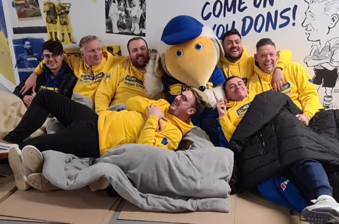 Sponsored participants cuddle up with AFC Wimbledon’s mascot on the stadium floor.