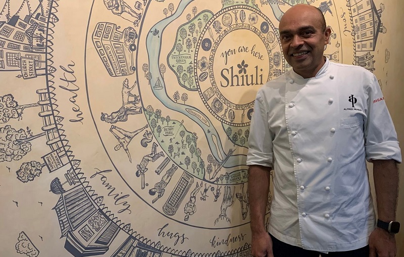 Chef Alfred Prasad, in this chef whites, stood next to a mural of Twickenham locations in Shiuli