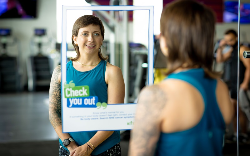 Woman in front of mirror looking at 'Check you out' cancer awareness sticker