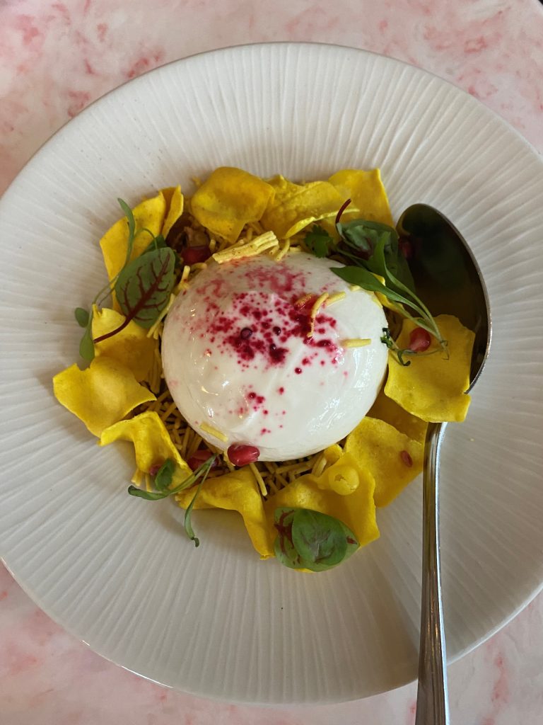 The restaurant't Burrata Chaat dish. A round piece of Burrata cheese on a bed of chickpeas, pomegrante and sev