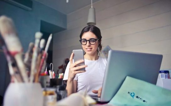 A woman checking her phone while working at her laptop