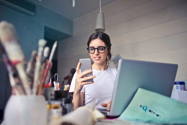 A woman checking her phone while working at her laptop