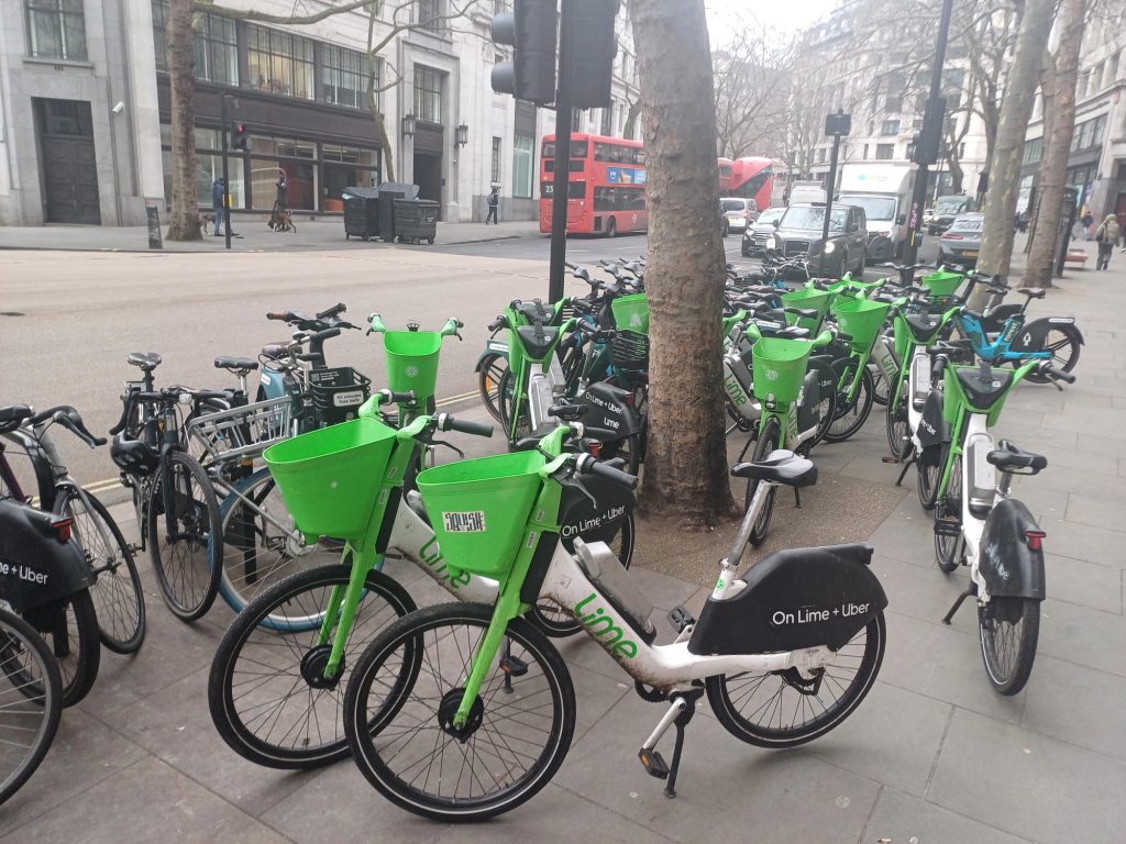 Dozens of Lime bikes parked alongside private bikes on a London street. 