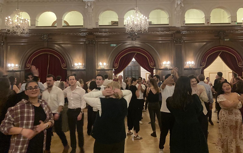 Ceilidh dancing in big hall with wooden arches, red cutains and chandeliers.