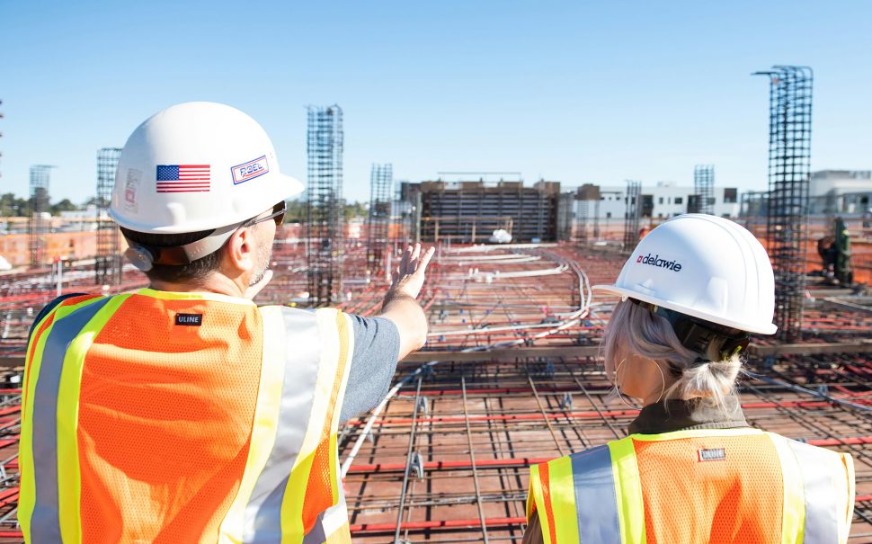 Man and woman in hard hats overlooking a building site