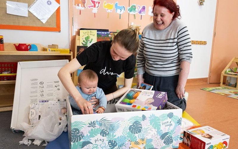 Two adults with a baby, playing with toys in a cardboard box