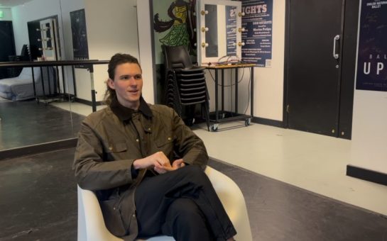 Picture of dancer Liam Woodvine sat in a chair with ballet studio behind