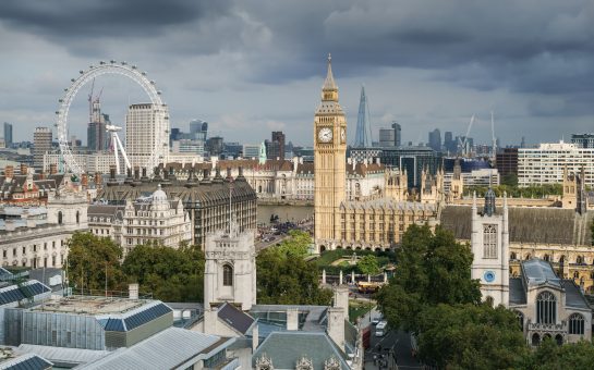 Landscape picture of London showing buildings such as Big Ben (a clock tower) and London Eye (observation wheel) with grey sky