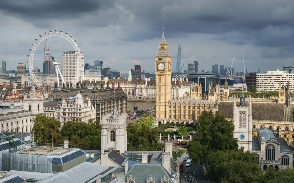 Landscape picture of London showing buildings such as Big Ben (a clock tower) and London Eye (observation wheel) with grey sky