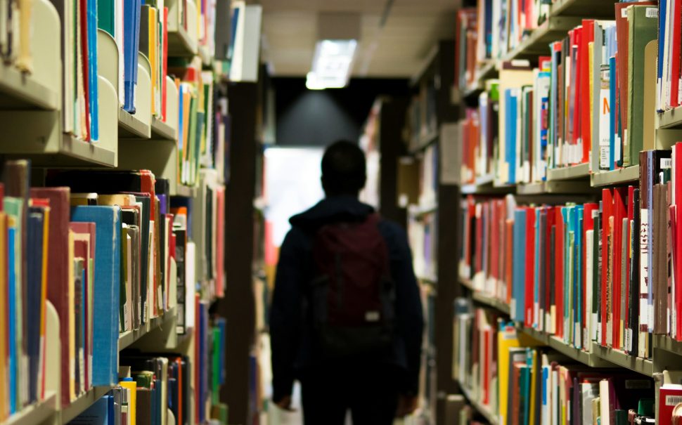 A silhouetted figure walks in between shelves at a university library.