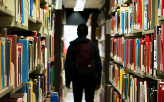 A silhouetted figure walks in between shelves at a university library.