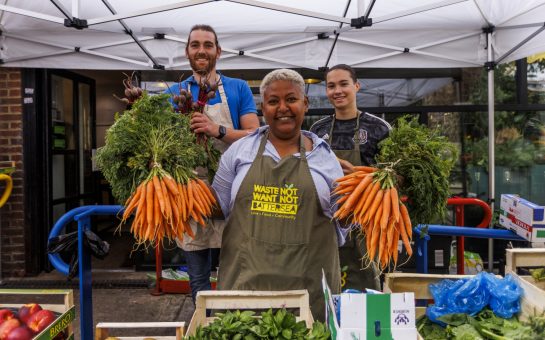 Smiling woman wearing g an apron holding carrots in both hands