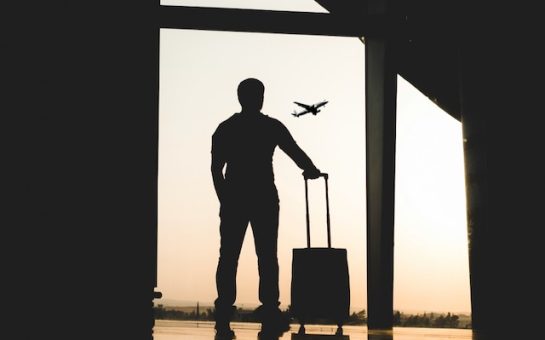 A man holding a suitcase looking at a plane from the airport window